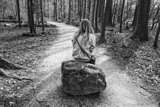 Junge Frau sitzt auf Stein auf einem Waldweg